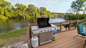 Una parrilla para barbacoa en una terraza con vista al río, un tanque de gas y una silla.