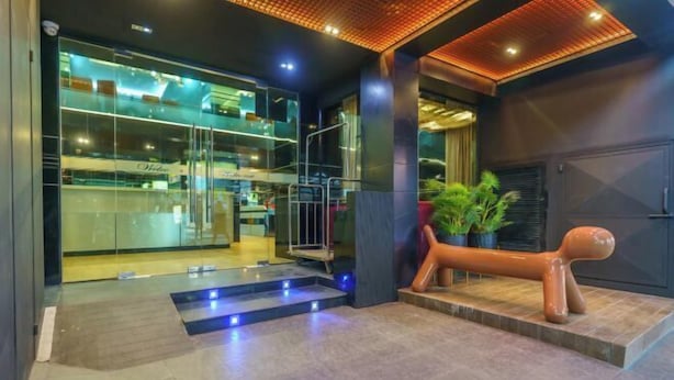 A modern hotel lobby with a glass facade, a staircase leading to the upper level, and a unique sculpture resembling a dog. - Deco Lux Hotel (Bangkok)