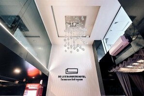 A modern hotel interior with a prominent chandelier, a reception desk, and a sign indicating the hotel name. - Deco Lux Hotel (Bangkok)