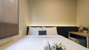 A neatly made bed with white linens, a headboard, and a bedside table with a lamp. - Deco Lux Hotel (Bangkok)