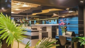 A modern office space with a blue and black color scheme, featuring desks, chairs, and potted plants. - Deco Lux Hotel (Bangkok)