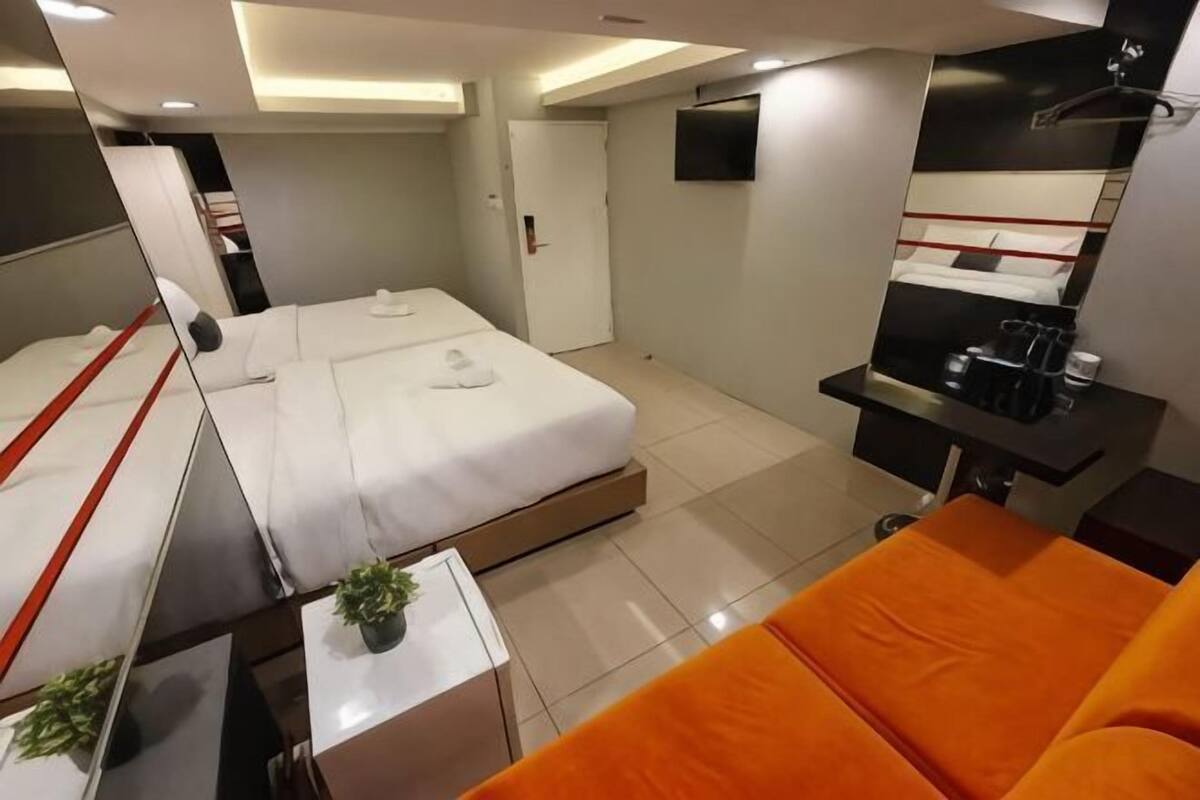 Une chambre d’hôtel avec un lit, un canapé, une petite table avec une plante, un miroir et une télévision.