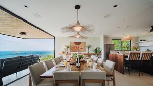 A dining area with a view of the ocean, a large table set for six, and a bar area with chairs. - Villa Zest 5 bedroom Villa • Rooftop Infinity Pool & Ocean Views (Quepos)