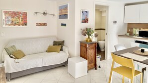 Ein modernes Wohnzimmer mit einer Couch, einem kleinen Tisch und einer Küchenzeile mit Esstisch und Stühlen.