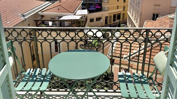 Ein Balkon mit rundem Tisch und Stühlen, mit Blick auf ein Wohngebiet mit mehrstöckigen Gebäuden.