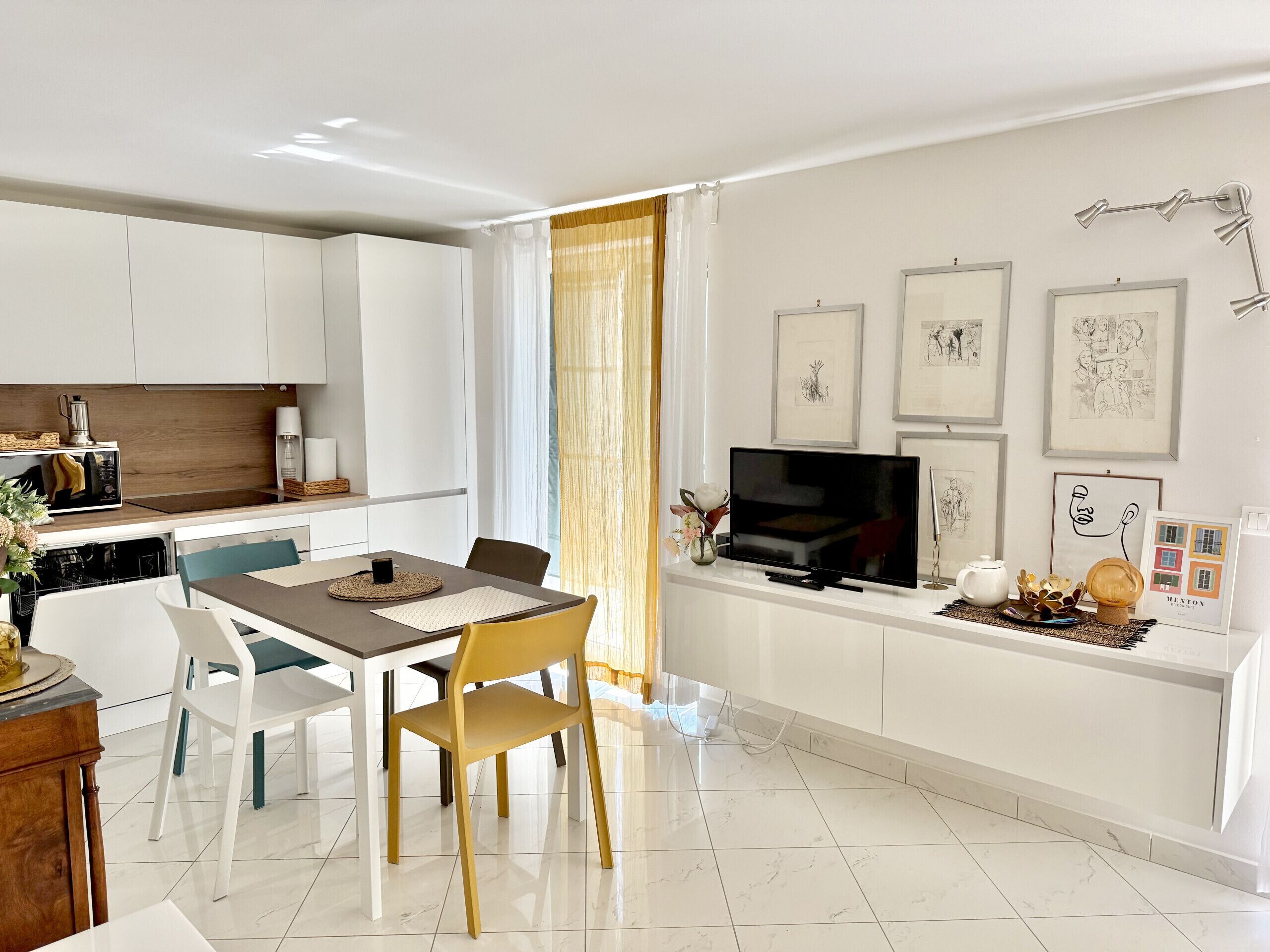 A modern kitchen with white cabinets, a dining area with a table and chairs, and a TV on a white stand.