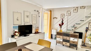 Ein modernes Wohnzimmer mit Flachbildfernseher, einem Esstisch mit Untertasse und einer Treppe mit Glastrennwand.