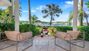 A covered outdoor seating area with wicker chairs and a small round table, overlooking a marina with boats and palm trees. - YACHT CLUB C3 - Contemporary One Bedroom Garden Level Condo over the Marina (Providenciales)