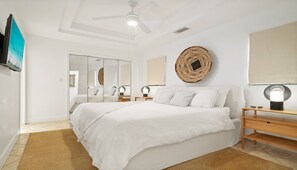 A bedroom with a large bed, a ceiling fan, a round woven wall hanging, and a mirror. - YACHT CLUB C3 - Contemporary One Bedroom Garden Level Condo over the Marina (Providenciales)