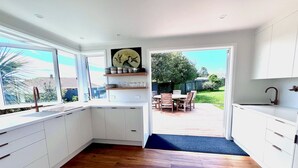 Una cocina moderna con armarios blancos, suelo de madera y vistas al patio trasero a través de amplios ventanales.