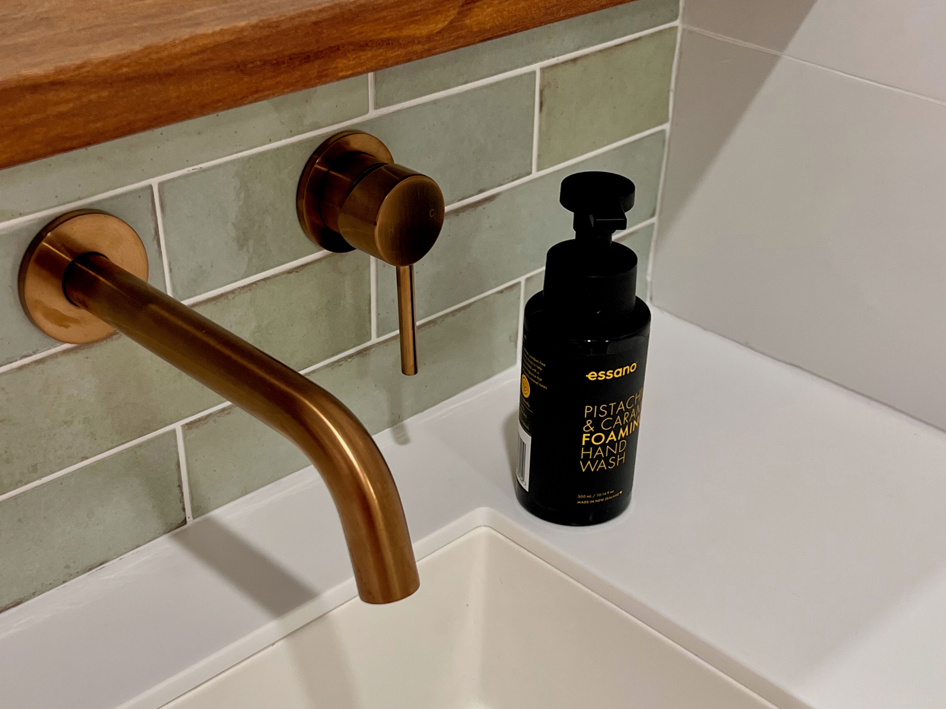 A bathroom with a white sink, a brass faucet, and a black bottle of hand wash soap.
