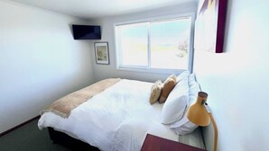 Una habitación de hotel con cama, ventana, televisor de pared y lámpara.