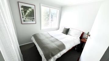 Une chambre à coucher bien rangée, avec un lit, une table de chevet, une lampe et une fenêtre équipée de stores.