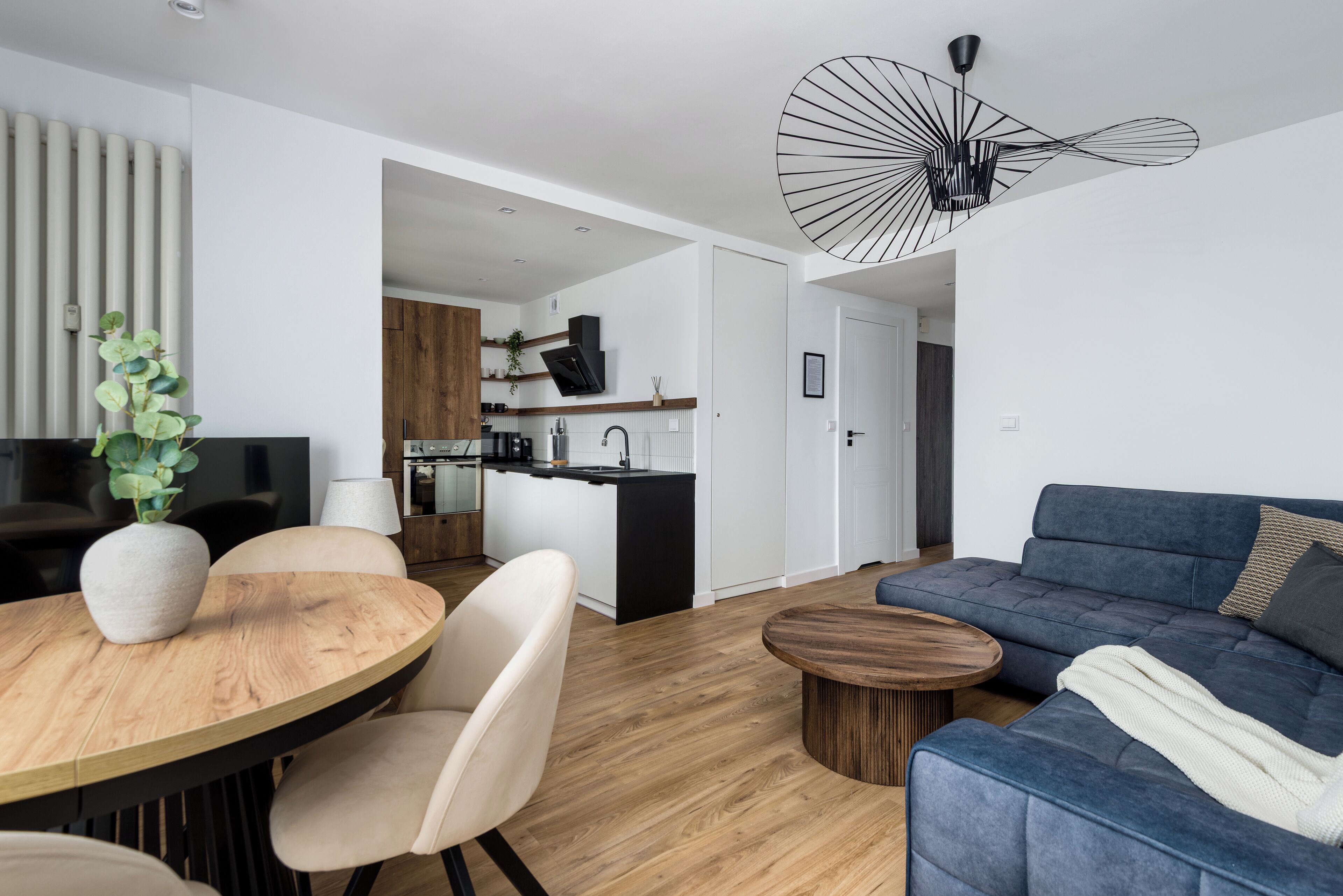 A modern living room with a wooden dining table, a blue sofa, and a unique ceiling light fixture.