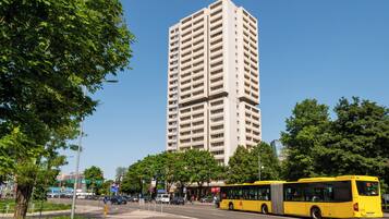Een gele bus op een stadsstraat, met een hoog gebouw op de achtergrond.