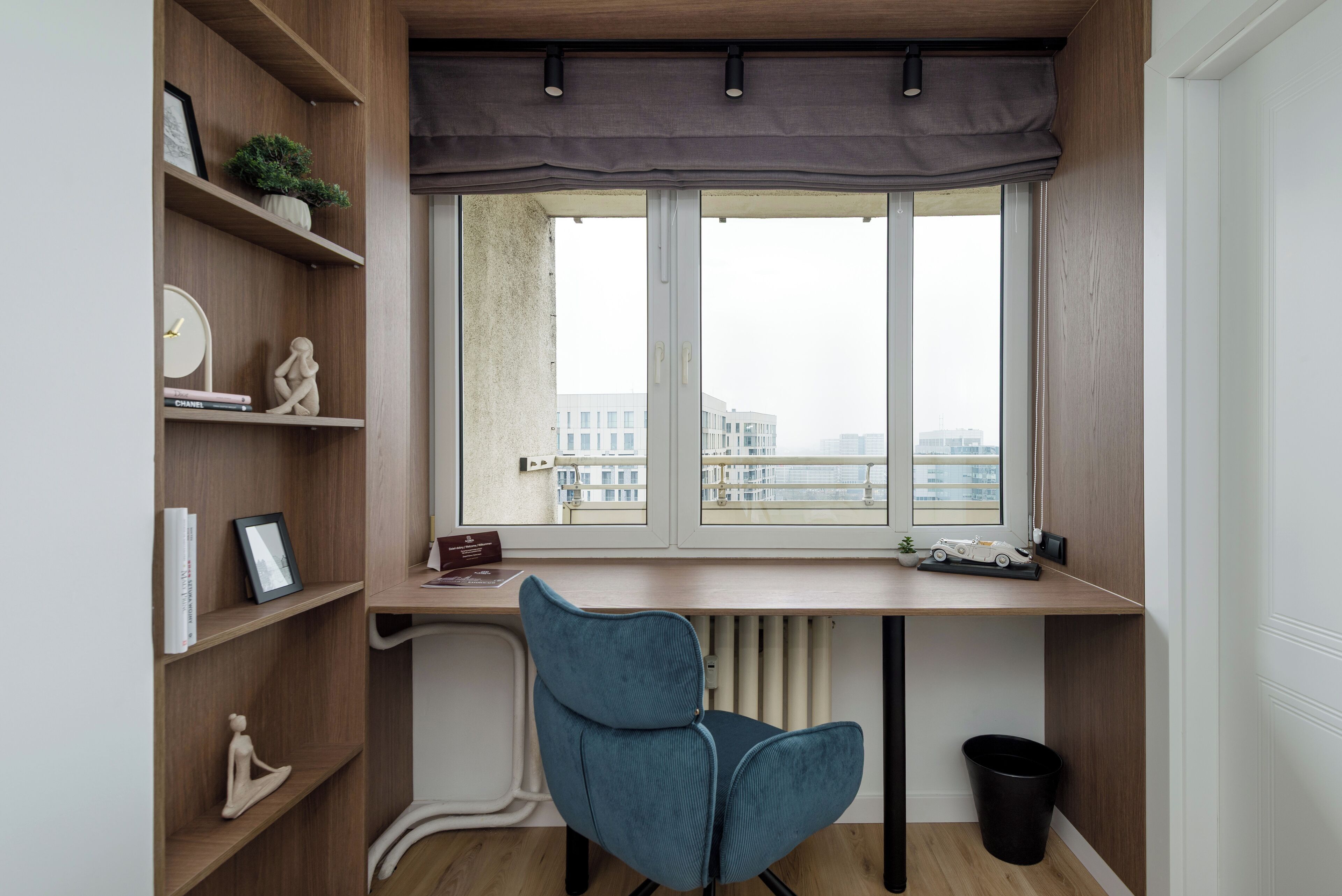 A modern workspace with a large window, wooden shelves, and a blue chair.
