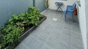 A small, enclosed patio area with a tiled floor, a blue chair, a small table, and a garden bed with green plants. - 5 bedroom house and courtyard - 1930's Roubaix (Roubaix)