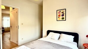Een slaapkamer met een bed, een nachtkastje, een aan de muur hangend schilderij en een deur die naar een andere kamer leidt.