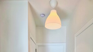 Een gang met een witte deur, een intercom op de muur en een lamp aan het plafond.