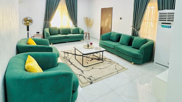 A modern living room with green sofas, a coffee table, and a large window with curtains. - Urban Ts (Abuja)