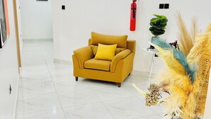 A hallway with a yellow armchair, a fire extinguisher, and a decorative plant. - Urban Ts (Abuja)