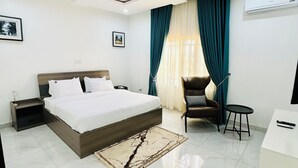 A modern bedroom with a large bed, a desk, a chair, and a small table. - Urban Ts (Abuja)