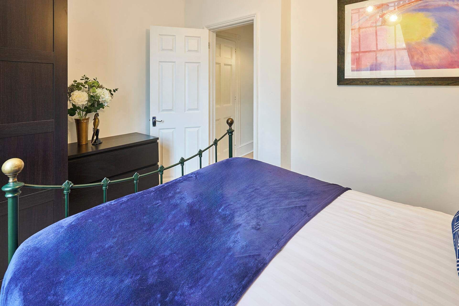 A bedroom with a bed, a dresser, a door, and a painting on the wall.