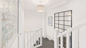 A staircase with white railings, a framed cityscape artwork, and a 'MEET ME AT THE BEACH' sign. - Host Stay The Coastal Retreat in Saltburn (Saltburn-by-the-Sea)