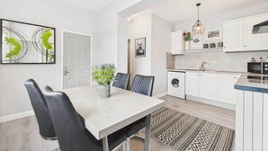 Una cocina moderna con armarios blancos, una zona de comedor con mesa y sillas, y una alfombra estampada.
