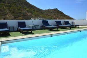 Una piscina con sillones de descanso y vistas a una colina.