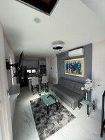 Uma sala de estar moderna com um sofá cinzento, uma mesa de centro de vidro e um quadro na parede.