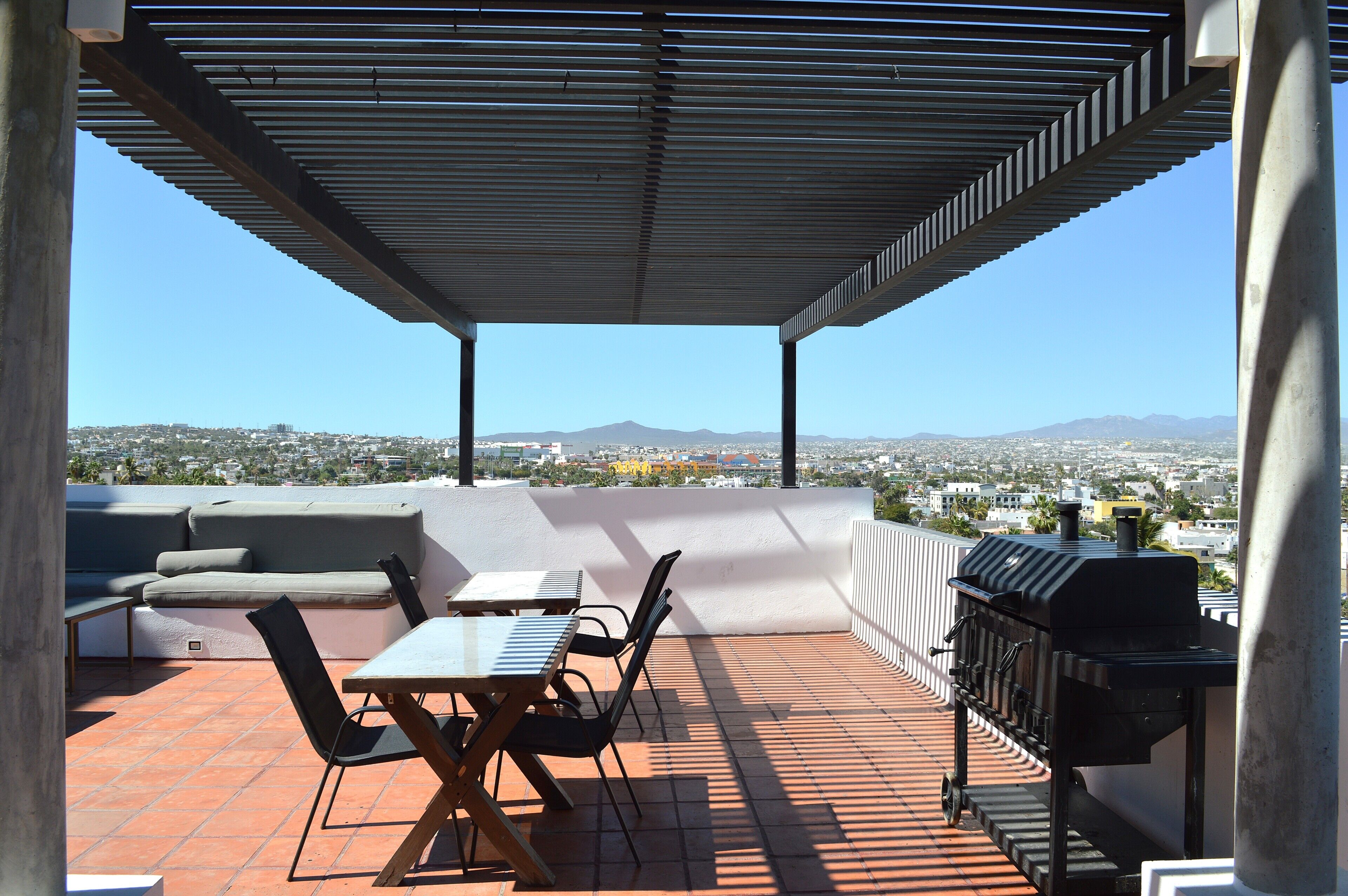 An outdoor patio with a table, chairs, a grill, and a view of a cityscape and mountains.