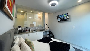 A modern hotel room with a bed, a sofa, a TV mounted on the wall, and a kitchen area visible through an open door. - The Residences Apart-Hotel By Morgan (Cabo San Lucas)