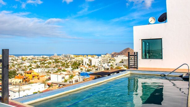 A rooftop infinity pool with a cityscape view, a modern building with satellite dishes, and a clear blue sky. - The Residences Apart-Hotel By Morgan (Cabo San Lucas)