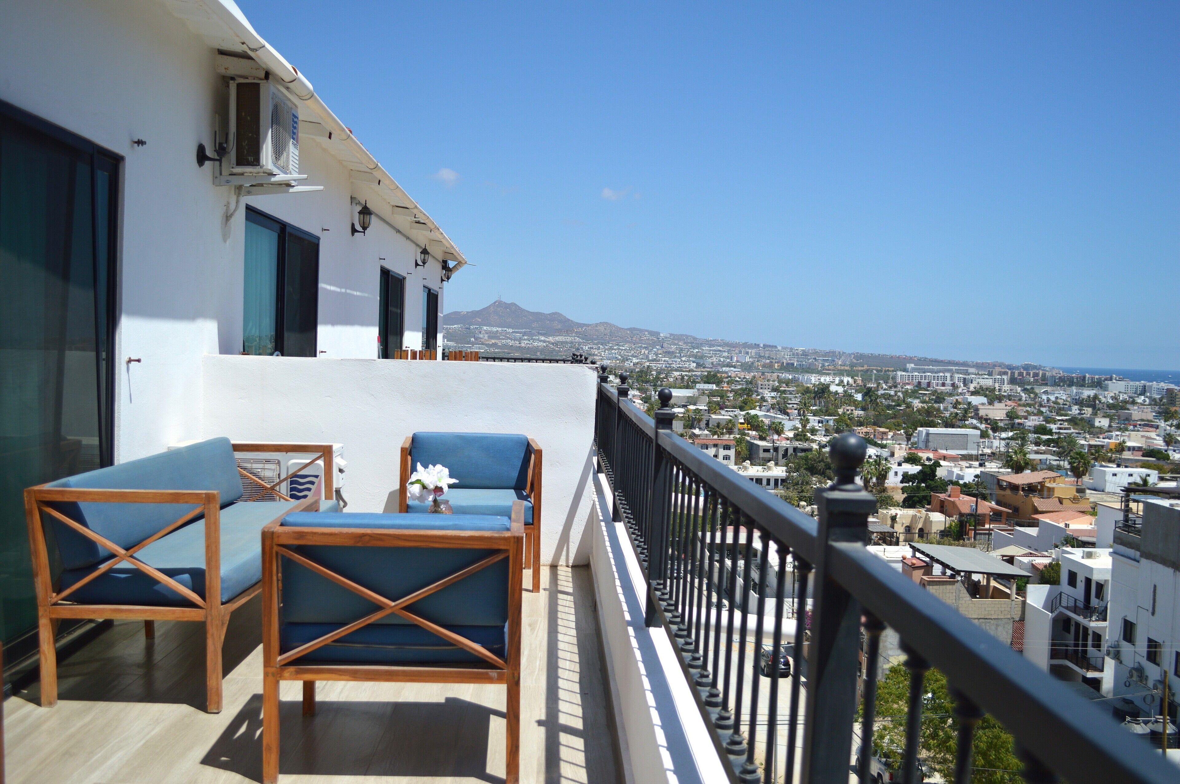 Ein Balkon mit zwei blauen Stühlen und einem kleinen Tisch, mit Blick auf eine Stadtlandschaft mit Gebäuden und einem Berg in der Ferne.
