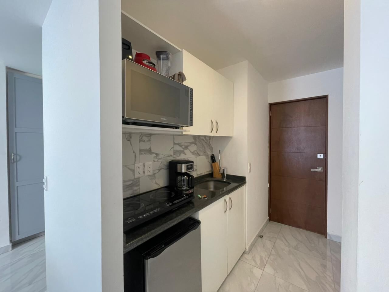 A compact kitchen with a microwave, coffee maker, and a sink.