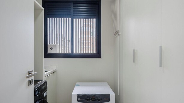 A compact laundry room with a washing machine, a dryer, and a window with blinds. - Apto Novo com 3 Suites a 600 m da Praia ELJ1201 (Itapema)