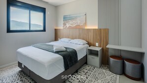 A modern bedroom with a large bed, bedside tables, a wall-mounted artwork, and a window with a view of the mountains. - Apto Novo com 3 Suites a 600 m da Praia ELJ1201 (Itapema)