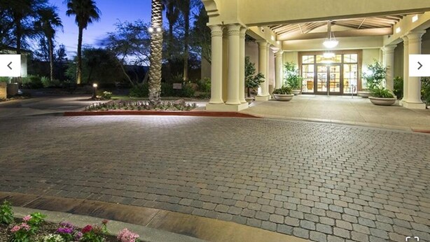 A hotel entrance with a covered walkway, palm trees, and a brick pathway leading to the doors.