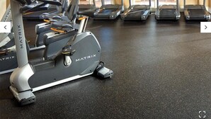 A gym with multiple treadmills and a stationary bike, with large windows allowing natural light.