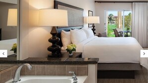 A hotel room with a large bed, a bathroom with a bathtub, and a view of a green landscape.