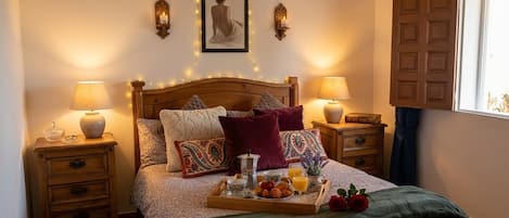 A neatly made bed with a tray of breakfast items, two bedside lamps, a framed picture above the bed, and a window with curtains.