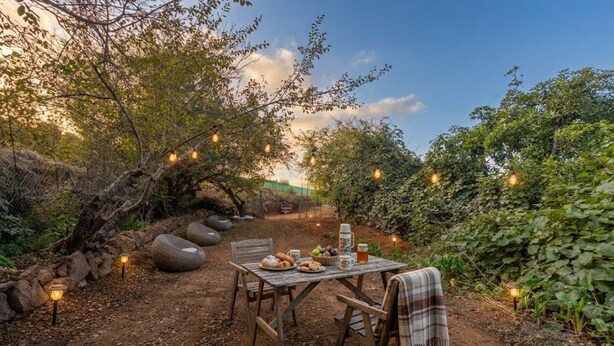 Zona pranzo all'aperto con tavolo apparecchiato per due, circondata da vegetazione naturale e sedute in pietra.