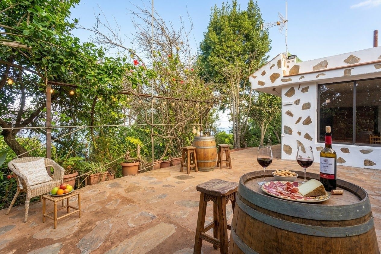Un patio al aire libre con una silla de mimbre, taburetes de madera, un barril de vino y una botella de vino.