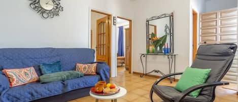 A living room with a blue sofa, a black chair, a small table with a tray of snacks, and a decorative mirror.