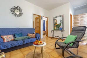 Ein Wohnzimmer mit blauem Sofa, einem schwarzen Sessel, einem kleinen Tisch mit einer Snackauswahl und einem dekorativen Spiegel.