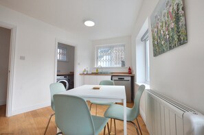 A compact kitchen with a window, a radiator, and a dining area with chairs. - Experience Cromer's coastal charm from this newly renovated, one bedroom apartment in the heart of C (Cromer)