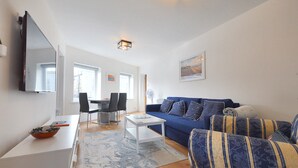 Ein modernes Wohnzimmer mit einem blauen Sofa, einem weißen Couchtisch und einem Essbereich mit Tisch und Stühlen.