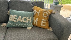 En grå sofa med to dekorative puder, hvor den ene har broderet "BEACH" og den anden "HOME".