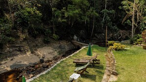 Un jardín con un pequeño arroyo, sillas de madera y una mesa.